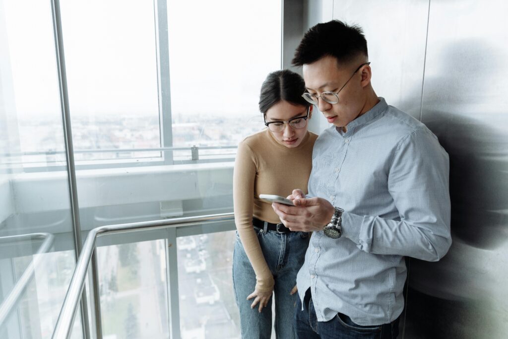 Elevator Downtime and Tenant Satisfaction two tenants looking at a phone in front of an elevator