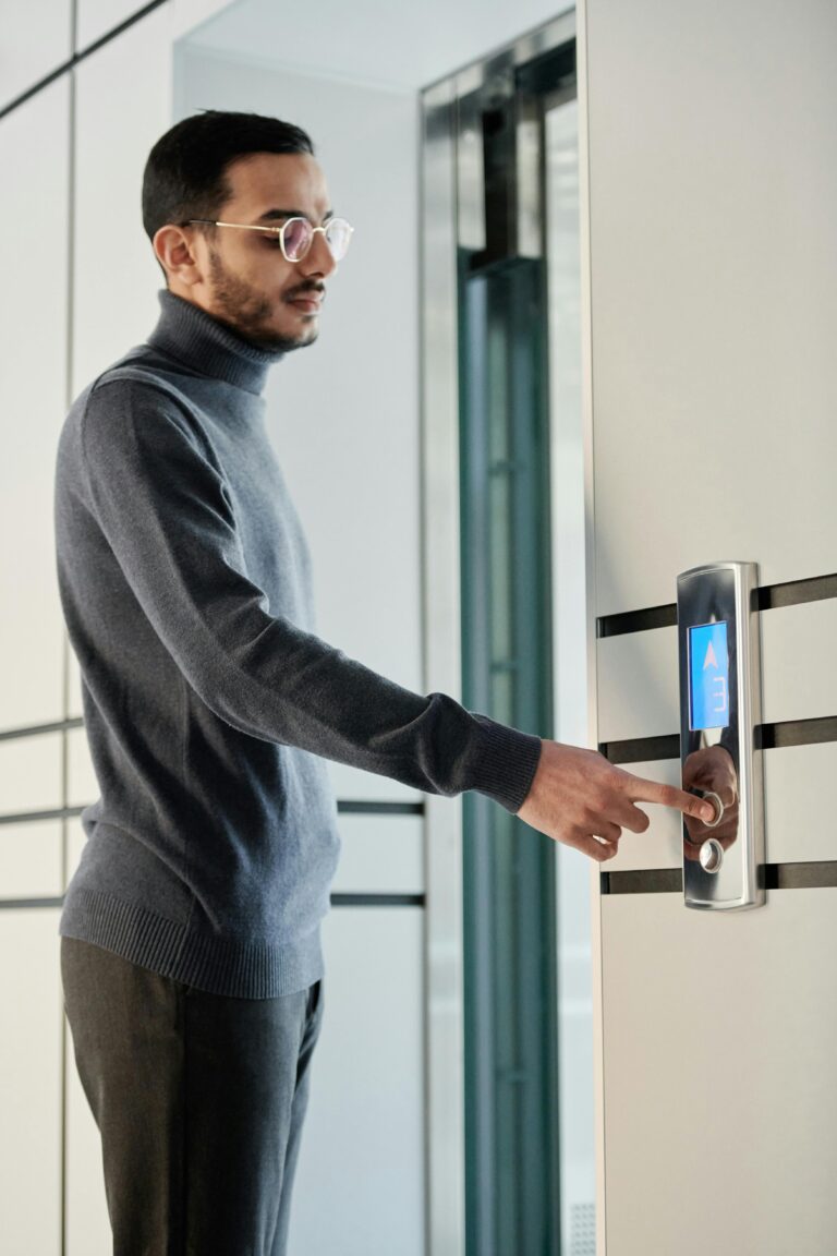 Five Signs That Your Elevator Monitoring System Needs an Upgrade man with glasses and gray pants and shirt pushing button outside an elevator