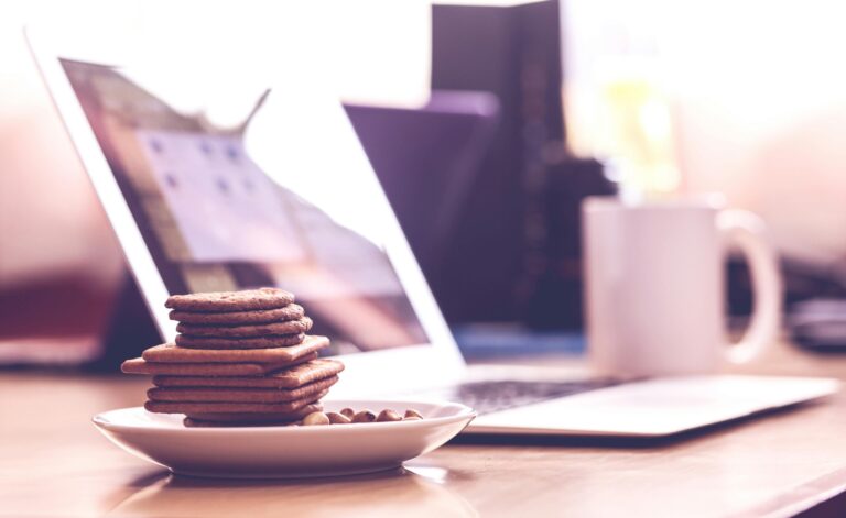 Cookie Notice a white plate stacked with cookies with a laptop in the background on a wooden table